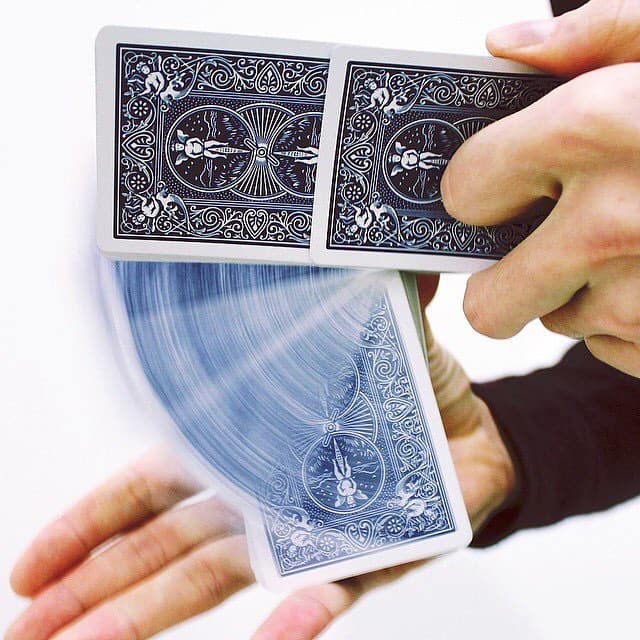 Two Bicycle-backed cards held between the fingers as a packet springs away beneath them in a blur.